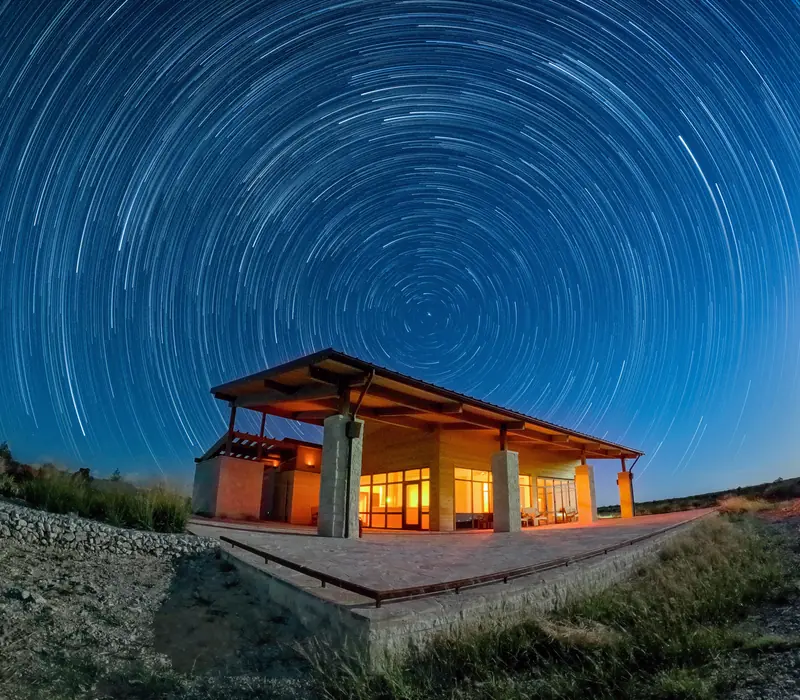 Glass-walled pavilion lit at night under star trails at Devils River State Natural Area, Texas