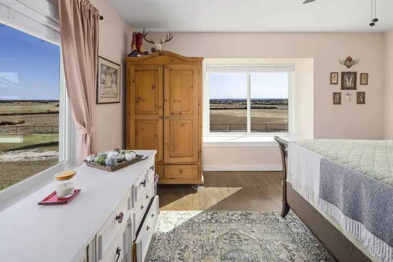 Bedroom with white sliding windows on two walls facing open pasture