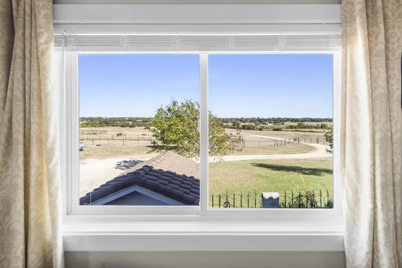 Wide white sliding window looking over the roof to the fields