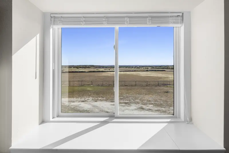 White sliding window set in a deep sill facing the pasture