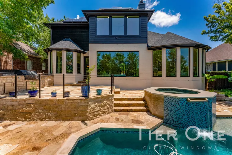 Rear of the home with window walls, a bay and a picture window above a pool and spa
