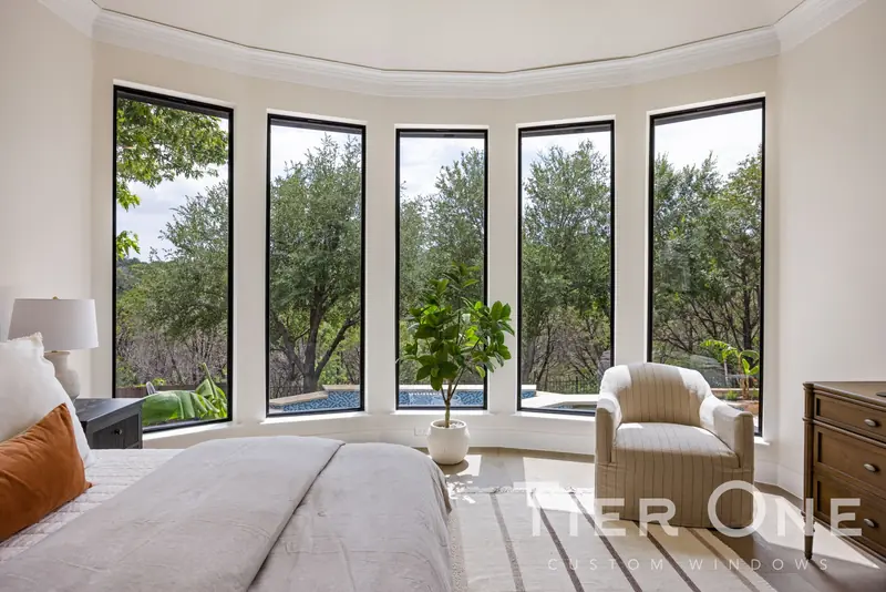 Curved bay of five tall black-framed windows looking into the trees
