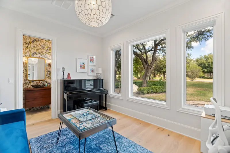 Piano room with tall white-framed windows facing the trees