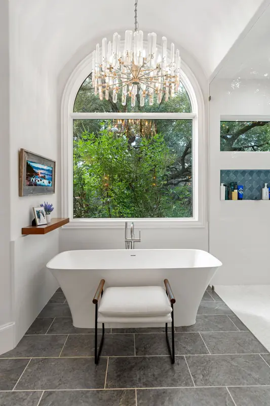 Arched window above a freestanding tub under a chandelier