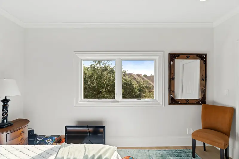 White-framed window pair in a bedroom looking onto oak trees