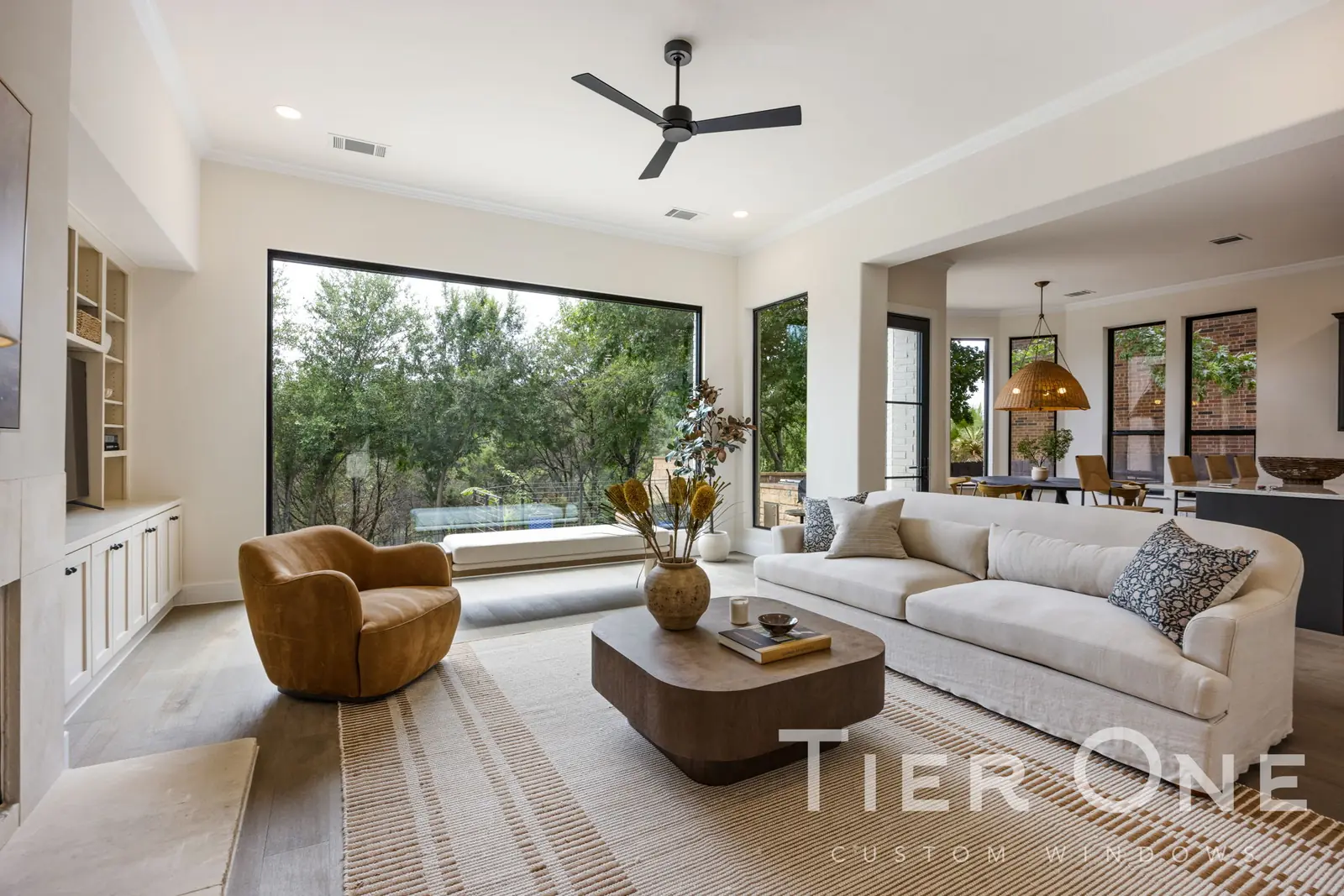 Large black-framed picture window in an open-plan living room looking onto oak trees