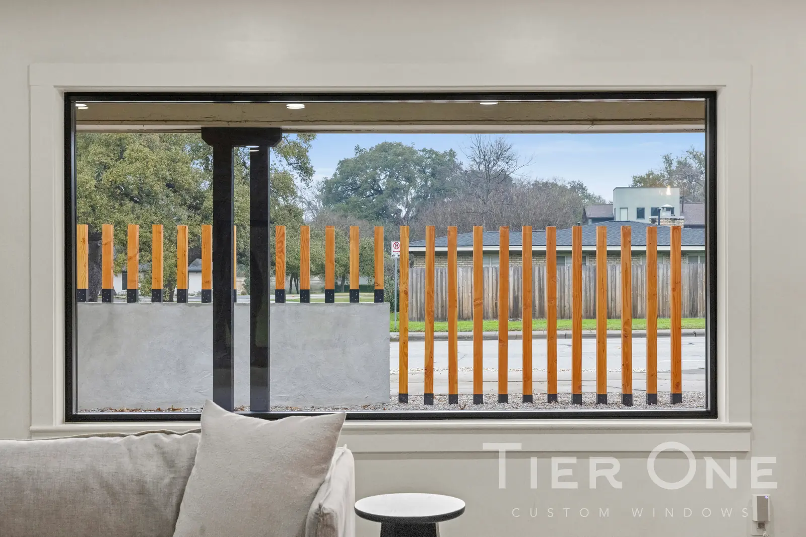 Wide black-framed picture window set behind a sofa looking onto a slatted fence