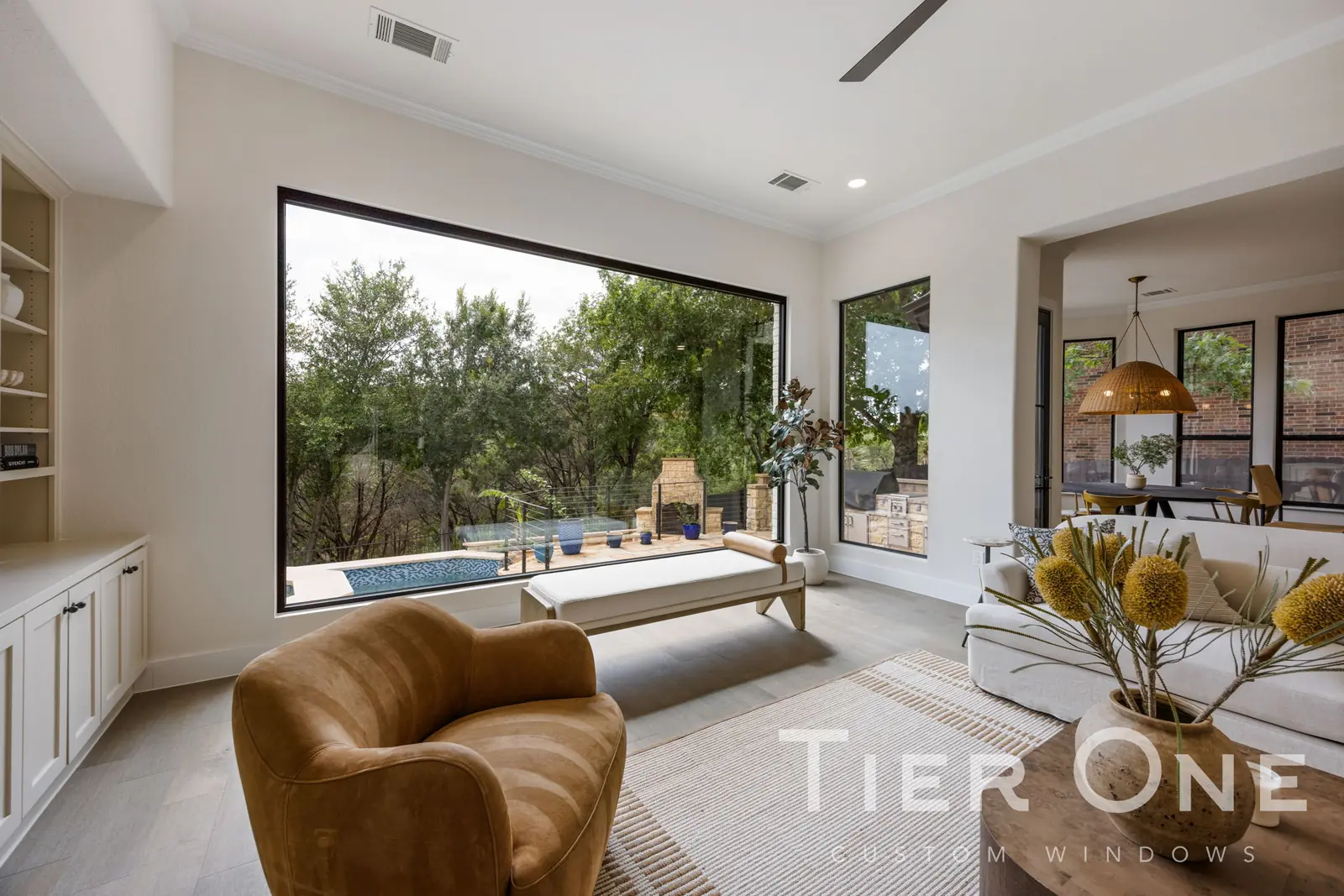 Large black-framed picture window in a living room looking onto a pool and treeline