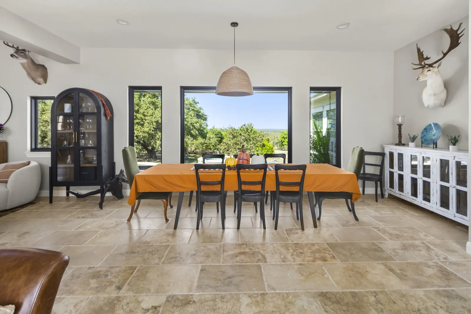 Run of black-framed windows and a door opening a dining room to a hill country view