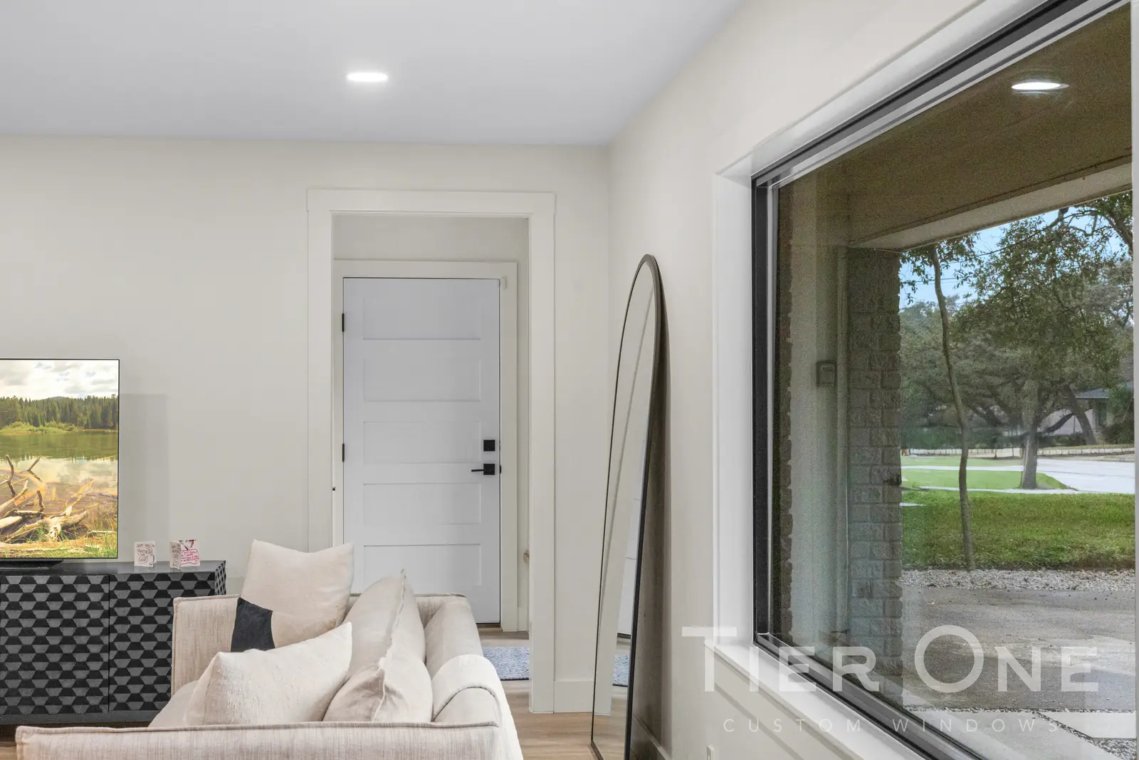 Black-framed picture window in a living room framing oak trees at the front of the house